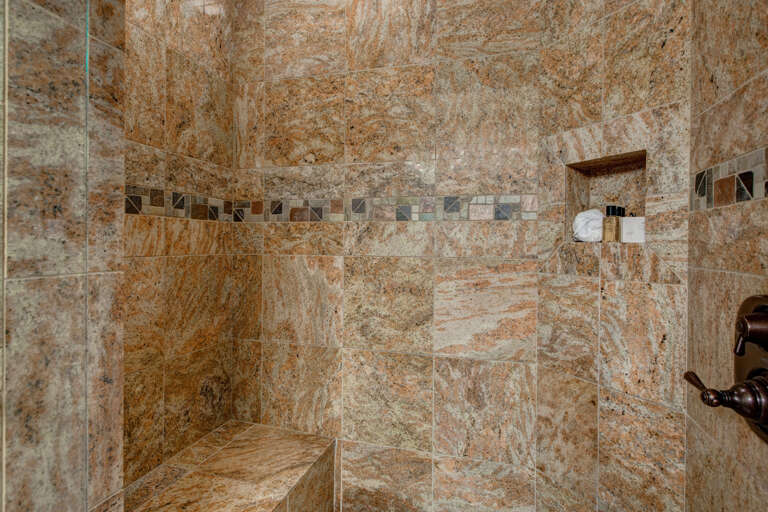 Step into your private walk-in shower with stunning granite tile, built-in bench seating, and a niche stocked with premium amenities for your ultimate relaxation.