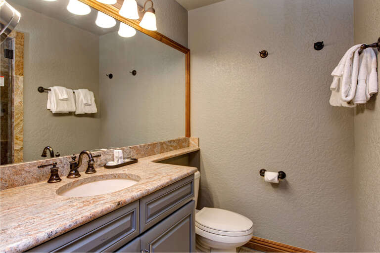 Step into your private bathroom with warm lighting, elegant granite countertops, plush towels, and a spacious mirror—a perfect spot to refresh each morning.
