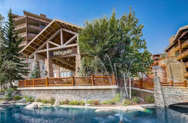 Westgate resort entrance features stone-and-timber architecture, landscaped grounds with mature trees, and a serene water feature at the property's arrival area.