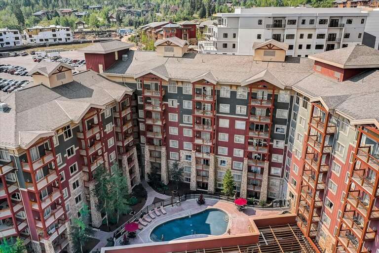 This aerial view showcases the property's distinctive horseshoe-shaped architecture embracing an inviting central courtyard pool, set against a backdrop of forested mountain slopes and neighboring resort buildings.