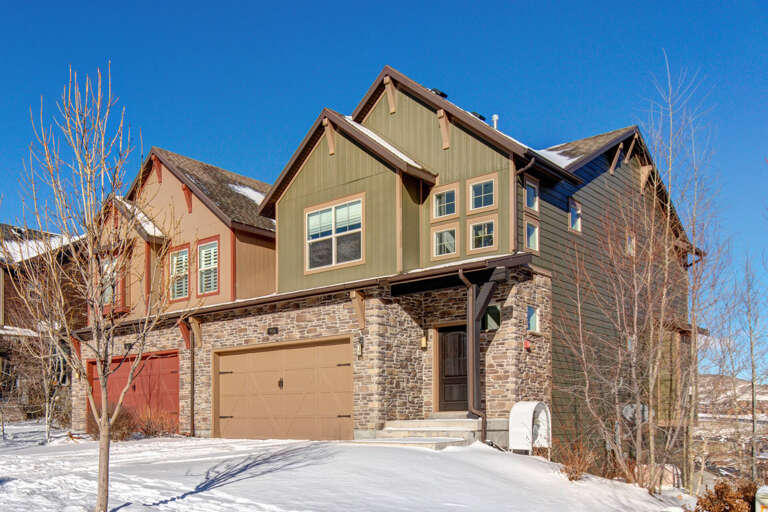 Modern mountain-style home with stone and wood exterior, positioned in a quiet neighborhood with stunning views and convenient access from a cleared, private driveway.