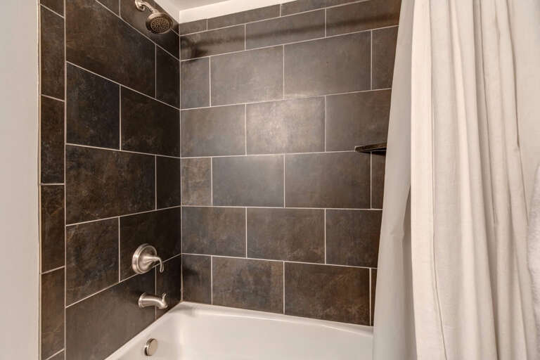 Sleek dark tile surrounds your private tub and rainfall shower, combining modern design with comfort for a truly rejuvenating experience.