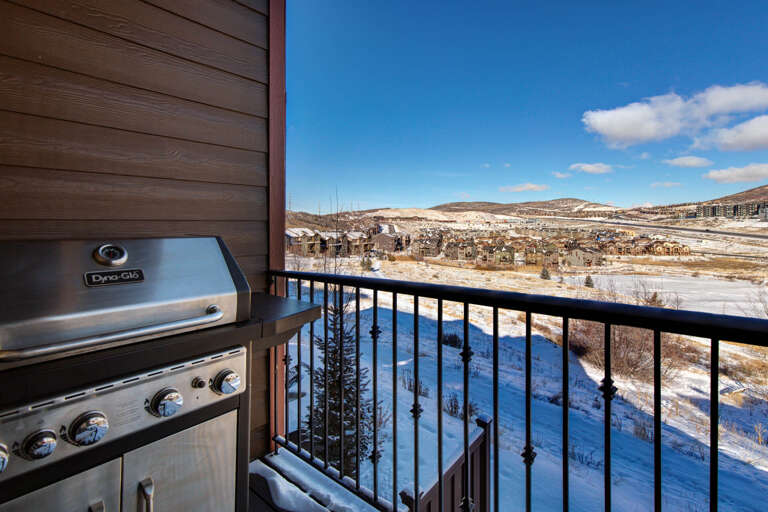 Private balcony with a gas grill offers sweeping views of snow-covered mountains and the surrounding valley below, perfect for year-round outdoor dining.