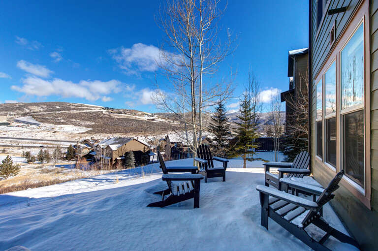 Peaceful snow-covered deck overlooking a scenic winter mountain valley and surrounding alpine neighborhood during daylight.