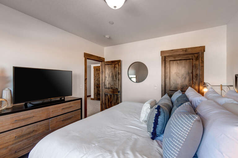 Unwind in your serene bedroom with plush bedding, warm wood accents, and modern amenities. Soft linens and a flat-screen TV await your comfort.