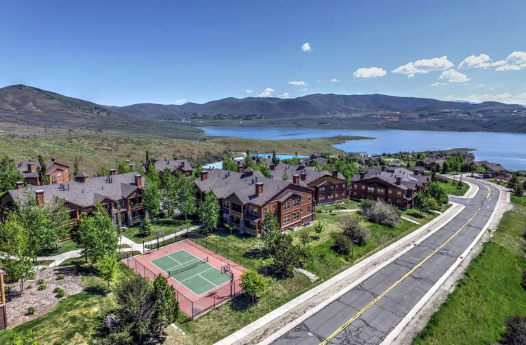 Scenic mountain resort community featuring multiple vacation homes, tennis courts, and walking paths, nestled along a pristine lake with sweeping mountain views.