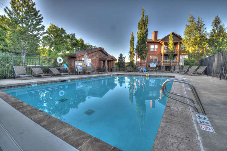 An outdoor pool surrounded by loungers and lush greenery offers a refreshing retreat. Nearby communal buildings and residential structures are visible in the late afternoon light.
