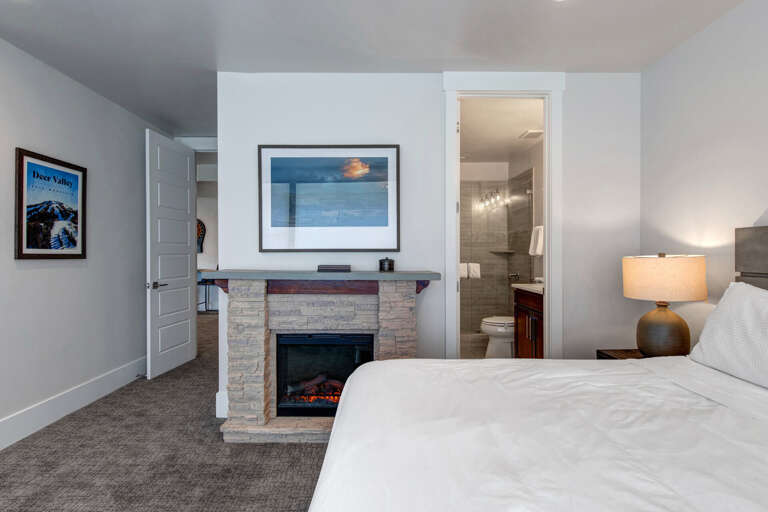 Unwind in your cozy bedroom featuring a stone fireplace for warmth and ambiance. The ensuite bathroom offers modern convenience, while soft lighting creates a serene retreat after a day of mountain adventures.