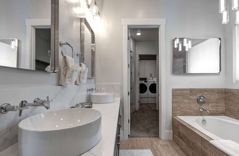 Your modern bathroom features dual vessel sinks, a luxurious soaking tub with wood-look accents, and contemporary lighting that creates a spa-like retreat for your stay.