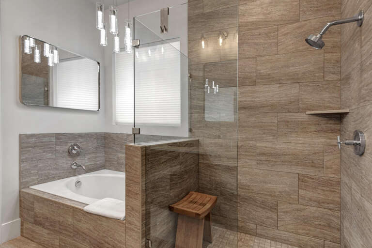 Unwind in your spa-inspired bathroom, where warm wood-grain tile embraces a sleek soaking tub and spacious glass-enclosed shower, creating your perfect retreat after exploring.
