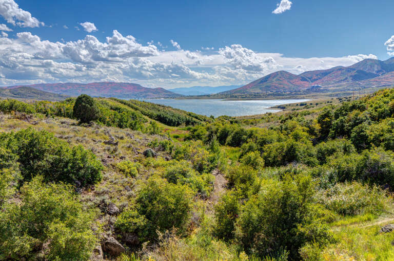 Scenic mountain landscape with rolling hills, lush greenery, and tranquil lake views under expansive blue skies—an idyllic natural setting near the property.