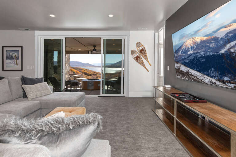 Your living area blends mountain charm with modern comfort, featuring plush seating, ambient lighting, and stunning alpine views through expansive doors that open to the outdoors.