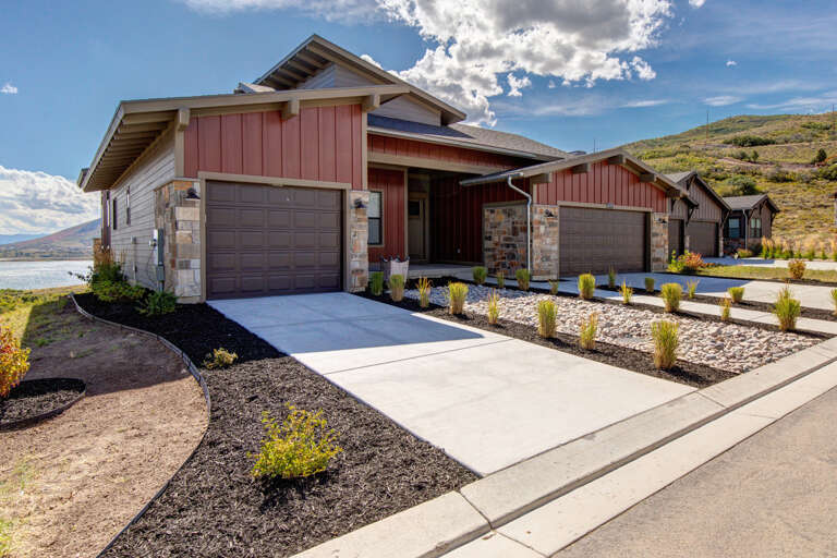 Modern vacation home exterior featuring ample parking, mountain backdrop, and waterfront location in a well-maintained residential community.