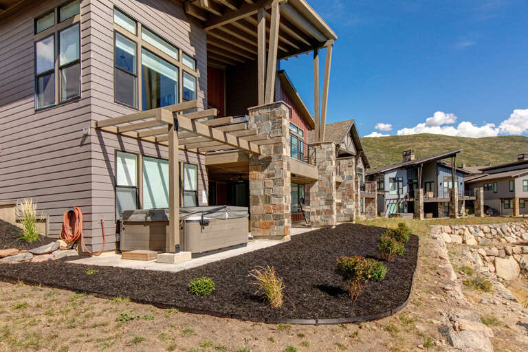 Modern mountain property featuring stone and wood architecture set against rolling hills. Multiple units visible, showcasing the property's exterior design and landscaped grounds under clear blue skies.