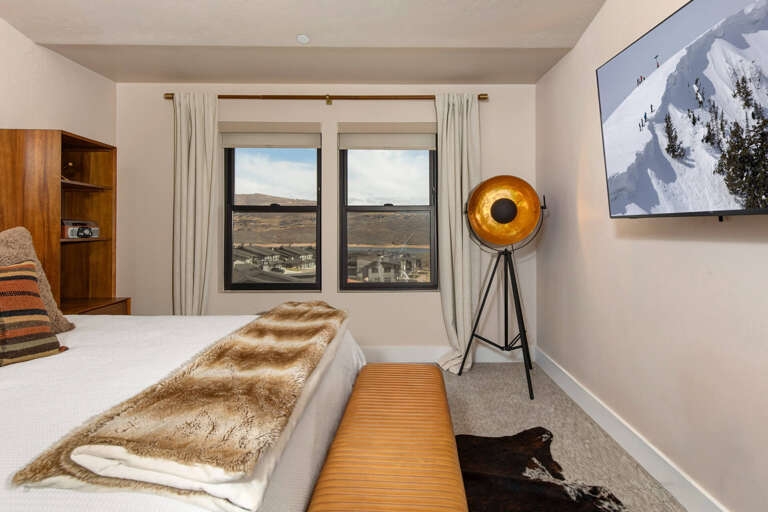Your cozy mountain retreat awaits with plush bedding, warm textures, and scenic views of the surrounding landscape stretching beyond your window.