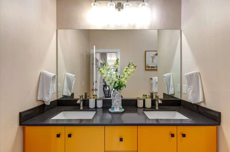 Step into your modern bathroom featuring a stylish double vanity with sleek black countertops and vibrant cabinetry. Fresh flowers and soft towels await your arrival.
