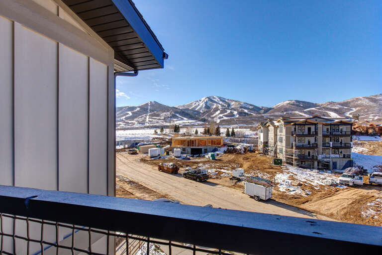 Mountain views overlook a developing neighborhood with ski slopes rising majestically in the distance, framing the arrival experience.