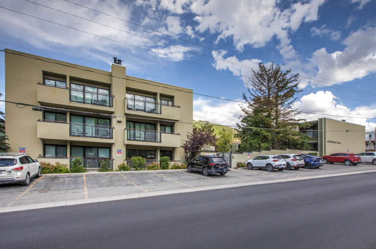 Modern three-story property featuring balconies with mountain views, surrounded by mature trees and convenient on-site parking for guests.