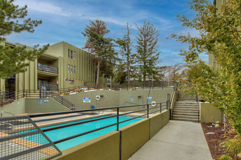 The property features a refreshing outdoor swimming pool surrounded by mature trees and multi-level architecture, offering a peaceful retreat in a landscaped setting with convenient stairway access.