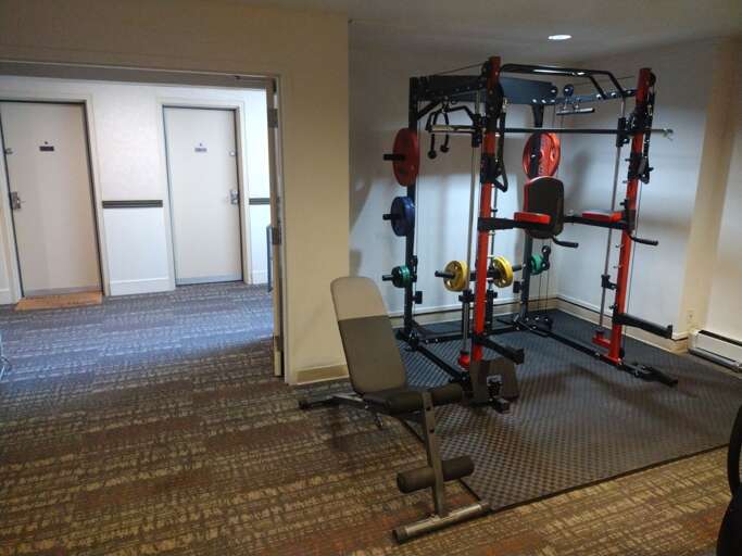Well-equipped fitness area ready for your strength training sessions, featuring a multi-station power rack with colorful weight plates and an adjustable bench for versatile workouts.