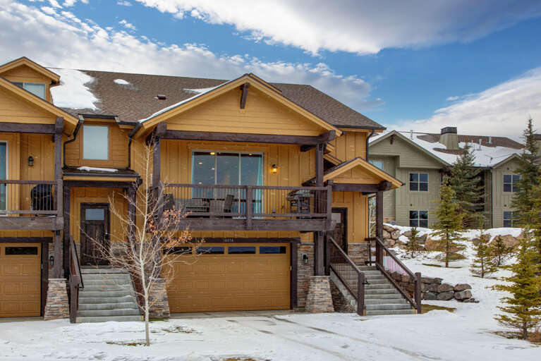 A charming mountain retreat surrounded by evergreens and snowy hillsides, featuring warm wood siding, spacious balconies, and convenient parking below.