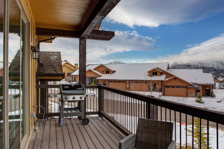 A covered deck overlooks a serene winter neighborhood with snow-dusted homes and majestic mountain peaks framing the horizon, offering a peaceful alpine setting year-round.