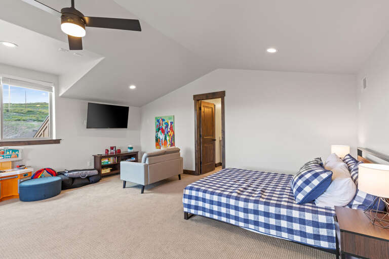 Your spacious bedroom welcomes you with vaulted ceilings, a cozy bed dressed in cheerful blue-checked linens, and a comfy lounge area perfect for unwinding after a day of adventure.