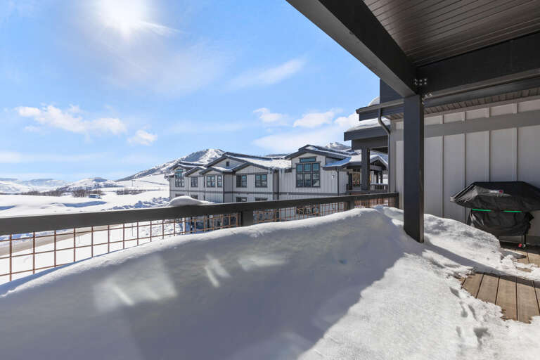 Modern mountain retreat with covered terrace overlooking pristine snow-blanketed valley and majestic peaks, featuring contemporary architecture and barbecue facilities for alpine gatherings.