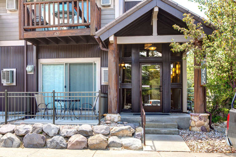 The entrance to your mountain retreat features rustic timber framing and a private balcony, offering a welcoming arrival experience surrounded by natural greenery and alpine charm.