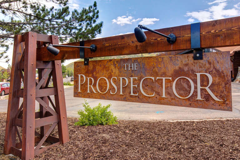 The property's entrance features a distinctive weathered-steel sign reading 'The Prospector,' flanked by industrial-style support structures and outdoor lighting against a bright daytime sky.