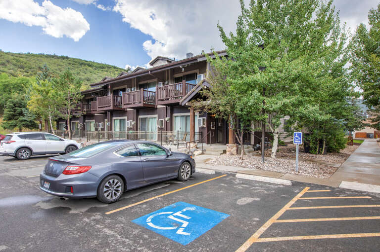 Mountain-view property nestled amid lush greenery with convenient parking including accessible spaces, featuring wooden balconies and a welcoming exterior framed by towering trees.