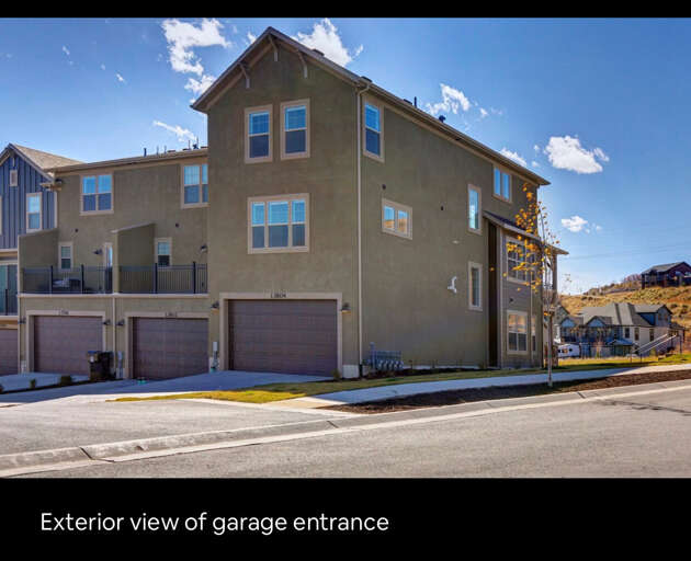 Modern townhome with spacious garage, nestled in a peaceful hillside neighborhood with blue skies and mountain views nearby.