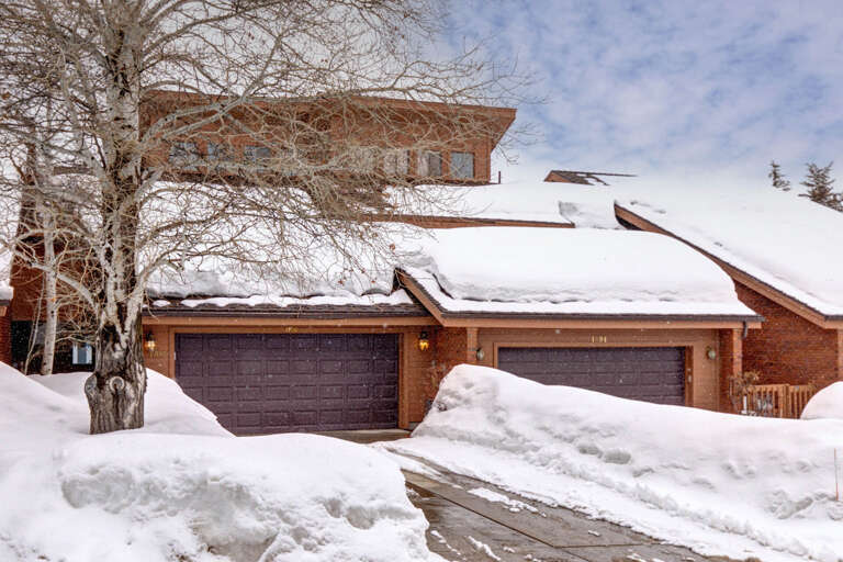 A brick vacation rental exterior with snow-blanketed roof and garage, nestled in a winter setting with a leafless tree in the front yard.
