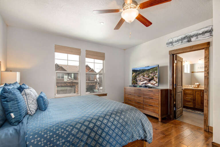 Drift off in comfort with a plush bed, ceiling fan, and TV. Your private en-suite bathroom awaits through the charming wooden door.