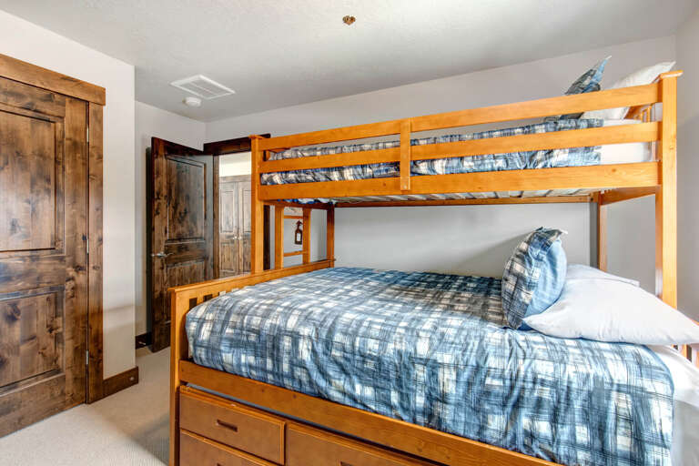 Perfect for families, this cozy bedroom features sturdy bunk beds dressed in charming plaid linens, rustic wooden details, and a built-in storage drawer for your belongings.