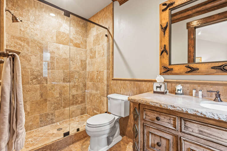 Unwind in your beautifully appointed bathroom featuring a spacious walk-in shower, elegant stone tile, and rustic wood accents that create a warm, mountain retreat atmosphere.