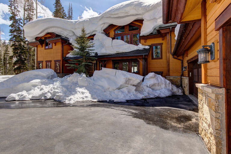 A stunning mountain retreat nestled among evergreens, showcasing dramatic snow-covered rooflines and warm wood architecture—a true winter wonderland escape in a pristine alpine setting.