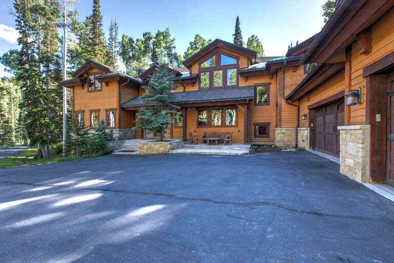 A mountain retreat featuring warm wood siding and stone accents nestled among towering evergreens with a spacious driveway and outdoor patio area.