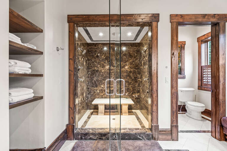 Step into your private spa-like retreat with a stunning walk-in shower framed by rich wood and dramatic marble walls—luxury awaits you here.