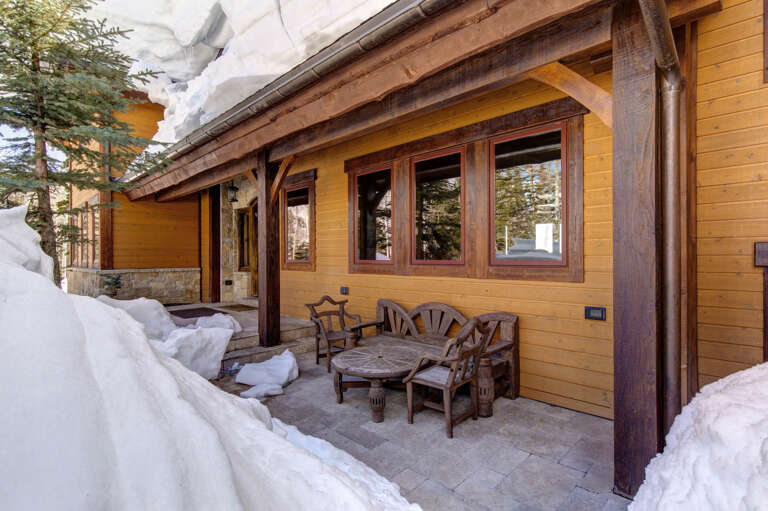 A cozy alpine hideaway with rustic wooden furniture awaits on your private covered patio, framed by fresh mountain snow and evergreens, perfect for morning coffee or evening relaxation.