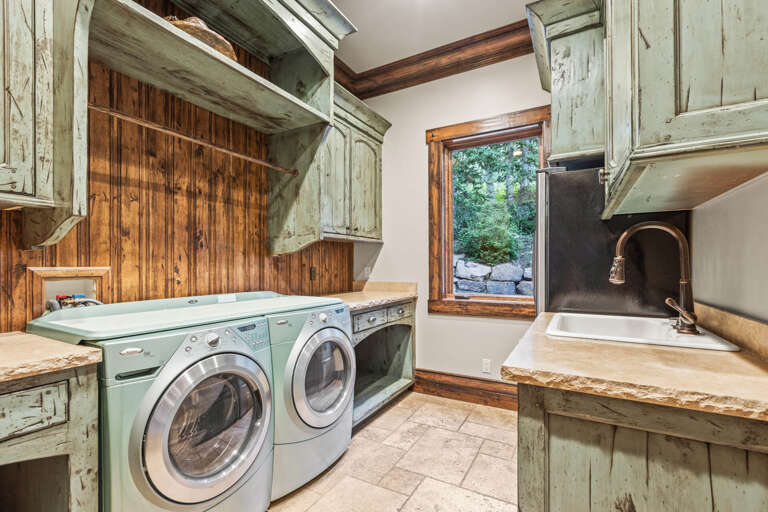 Your laundry day transforms into a peaceful retreat in this charming space with rustic cabinetry, warm wood accents, and serene garden views through the window to keep you company.