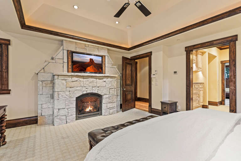 Your spacious bedroom features a stunning stone fireplace with warm glow, rich wood accents throughout, and inviting vaulted ceilings that create an elegant mountain retreat.