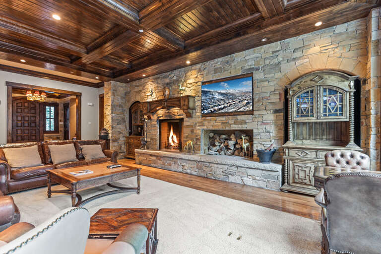 Sink into luxurious leather seating beside a crackling stone fireplace under stunning wood-beamed ceilings—your perfect mountain retreat awaits.