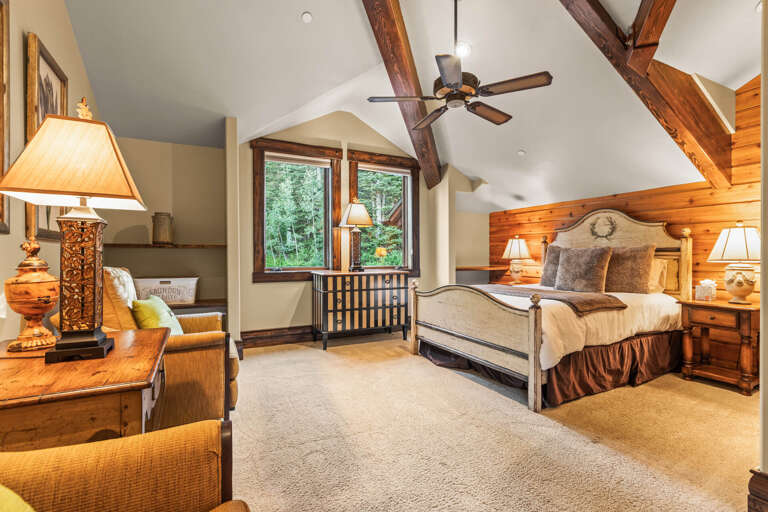 Your spacious bedroom features vaulted ceilings with rustic wooden beams, a plush bed, and cozy seating where you can unwind while gazing at serene forest views.