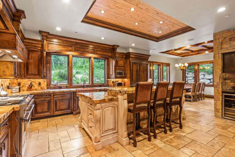 Your dream kitchen awaits with rich wood cabinetry, granite countertops, and a center island perfect for gathering. Natural light streams through large windows overlooking lush greenery, while recessed lighting highlights elegant wood-beamed ceilings.