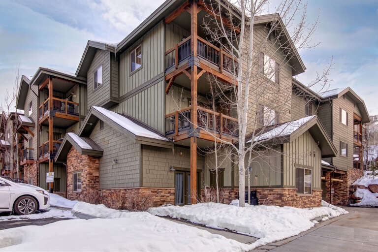The property features mountain-style architecture with warm wood accents and spacious balconies, nestled in a scenic winter setting with convenient parking access.