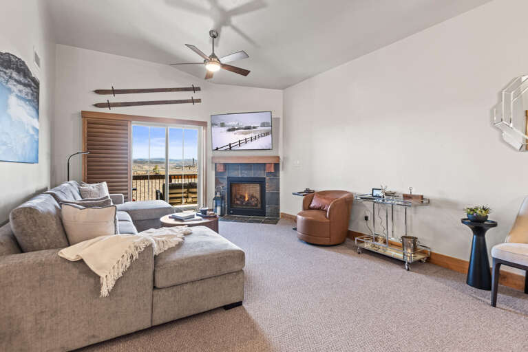 Relax in your bright living room where a cozy fireplace sets the mood and a private balcony opens to mountain views beyond. Unwind on plush seating beneath vaulted ceilings—your perfect retreat awaits.