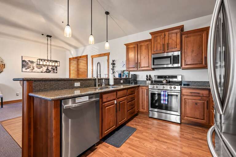 Your fully equipped kitchen awaits, complete with warm wood cabinetry, granite counters, stainless appliances, and a breakfast bar for casual meals together.