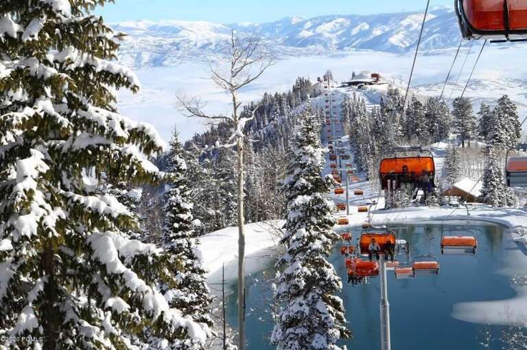 A pristine ski resort surrounded by snow-covered peaks and evergreen forests. Ski lifts transport guests above a serene pond, with mountain views stretching to the horizon.