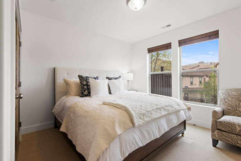 Sink into this plush bed with soft linens and layered pillows while natural light pours through windows framing desert vistas and bright skies—your perfect retreat awaits.